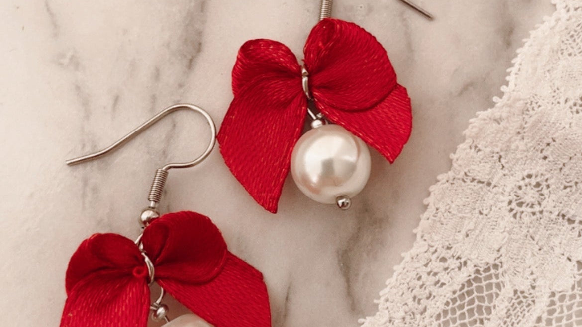 Red bow earrings with pearl centers on a marble surface